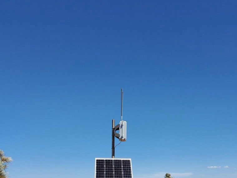A solar-powered LoRaWAN gateway and antenna mounted on a pole against open sky